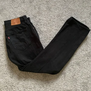 Svarta Levi's 501 jeans W33 L30 - Svarta Levi's 501 jeans med klassisk rak passform och femficksdesign. Jeansen har hög midja, ikonisk läderpatch bak och är tillverkade i slitstarkt bomullstyg. Perfekta för dig som gillar en tidlös och clean look.