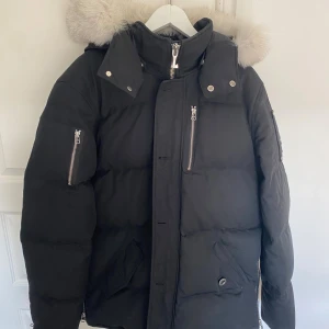 Svart dunjacka med päls från Moose Knuckles - Säljer en svart dunjacka från Moose Knuckles med fluffig ljus päls runt huvan i strl XL. Perfekt för kalla vinterdagar. Har kvitto och tagsen kvar. Väldigt bra skick. Priset är ej hugget i sten.