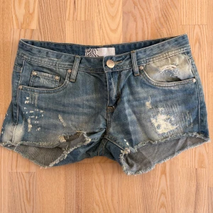 VS Miss jeansshorts - Snygga blå jeansshorts från VS Miss Jeans med slitna detaljer, fransig kant och klassisk femficksmodell. Shortsen har låg midja. 