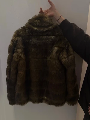 Brun pälsjacka från NLY Trend - Säljer en fluffig och snygg brun pälsjacka från NLY Trend i storlek 38. Jackan har en bred krage och är helfodrad, perfekt för att hålla värmen. Den har en cool, lite oversized look och är supermjuk med ett lyxigt pälsmaterial.