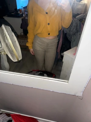 Gul croppad kofta från 157 - Säljer en snygg gul croppad kofta från 157 med grovstickad struktur och stora svarta knappar framtill. Koftan har v-ringad hals och långa ärmar med breda muddar. Perfekt för dig som gillar trendiga och bekväma plagg med lite loose passform.