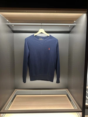 Mörkblå tröja från Polo Ralph Lauren - Snygg mörkblå tröja från Polo Ralph Lauren i storlek S. Klassisk design med rund hals och lång ärm, samt den ikoniska broderade loggan i rött på bröstet. Tillverkad i mjuk bomull som är skön mot huden. Perfekt för dig som gillar stilrena och tidlösa plagg. Hör av er vid frågor eller funderingar som vanligt är priser ej hugget i sten