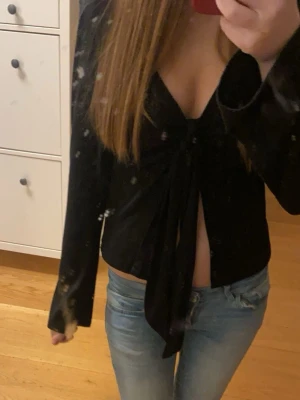 Svart omlottopp med knyt framtill - Säljer en svart omlottopp från Gina Tricot med lång ärm och djup v-ringning. Toppen har snygg knytning framtill som ger en croppad look och är tillverkad i mjukt, stretchigt material. Perfekt att styla med jeans eller kostymbyxor.