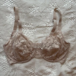 Ljusrosa spets-bh - Säljer en ljusrosa bh med vacker spets och blommigt mönster. Den har justerbara axelband och tre hyskor i ryggen för perfekt passform (ser mer beige ut på bilden).🦢