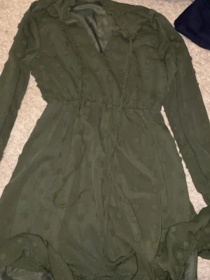 Grön prickig kortklänning med snörning - Supersöt grön kortklänning med prickigt mönster och långa ärmar. Klänningen har snörning i midjan och en lätt v-ringning. Tunt, flowy material som känns luftigt och skönt. Perfekt för dig som gillar en chill men ändå snygg stil.