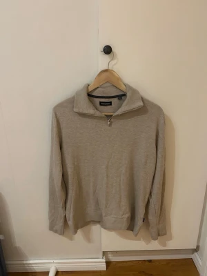 Beige half zip tröja från Jack & Jones - Säljer en beige långärmad tröja från Jack & Jones med half zip framtill. Tröjan har en hög krage och är tillverkad i mjukt stickat material som känns skönt mot huden. Perfekt för lager-på-lager och chill dagar. Snygg och enkel att matcha med jeans eller chinos.