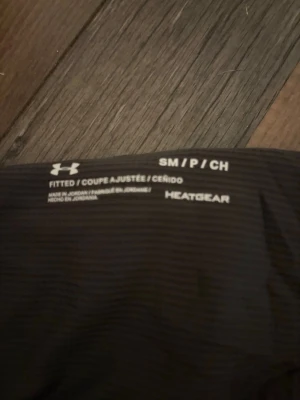 Svarta träningsshorts från Under Armour - Säljer ett par svarta träningsshorts från Under Armour i storlek S. De har en loose passform och är tillverkade i syntetmaterial med HeatGear-teknologi som håller dig sval. Perfekta för gymmet eller löpning, med elastisk midja och diskret logga på benet. aldrig använda!