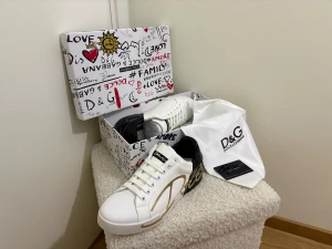 Dolce & Gabbana vita sneakers med guld - Säljer ett par snygga Dolce & Gabbana sneakers i vitt skinn med svart häl och guldigt grafiskt tryck på sidan. Skorna har rund tå, platt sula med mönstrad undersida och klassisk snörning. Kommer med originalkartong, dustbag och äkthetskort.