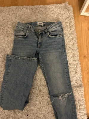 Bootcut jeans från 157 med slitning - Bootcut jeans från 157 i ljusblå tvätt med låg midja. Klassisk femficksmodell och slitning med hål på ena knät för en cool, avslappnad vibe. Materialet är jeans och passformen är loose med bootcut-stil. Perfekt för dig som gillar en laidback look.