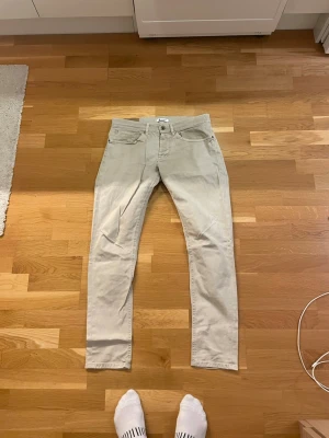 Beige Dondup chinos i slim fit, storlek 33 - Säljer ett par snygga beige chinos i slim fit med klassisk femficksdesign. Byxorna har en rak och smal siluett, passande för dig som gillar stilrena och enkla plagg. Materialet är mjukt och bekvämt, perfekt för dig som vill ha en clean look.