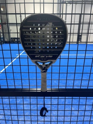 Starvie Tritón padelracket - Starvie Tritón padelracket med teardrop-form och längre handtag, tillverkat i Spanien. Racketen har en svart och vit design med kolfiberyta (Carbon 3K) och EVA Ultra Soft kärna. Perfekt för dig som vill ha full plane effect och snygg look på banan.