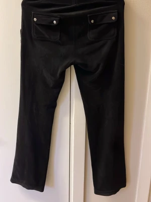 Juicy couture mjukis byxa  - Svarta mjukisbyxor med raka ben och snörning i midjan. Byxorna har stora fickor både fram och bak med knappdetaljer på bakfickorna. Materialet ser ut att vara mjukt och bekvämt, perfekt för chill dagar. Snygg och enkel design som funkar till många stilar.