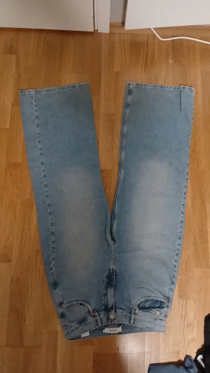 Ljusblå raka jeans från junkyard - Säljer ett par ljusblå jeans från Uniqlo med klassisk femficksdesign och baggy ben. Jeansen har en enkel, ren look med ljusa tvättade partier och rå kant längst ner på benen. Perfekt för dig som gillar en chill och avslappnad stil.
