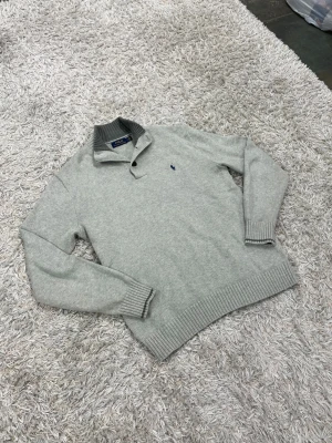 Polo Ralph Lauren tröja 1/4zip med knapp grå storlek M - Väldigt snygg grå 1/4 zip med knappar från Ralph lauren. En stickad tröja som är perfekt för komfort och stil🙌 storlek M men passar bra dem som bär L också. och är i ett otroligt fint skick utan några skador alls✅✅ vid frågor/prisförslag tveka inte med att höra av dig😇OBS KOLLA IN FÖERA LIKNANDE PLAGG I PROFILEN.