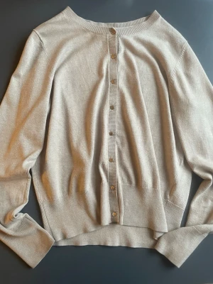 Beige kofta från Holly & Whyte  - Snygg beige kofta från Holly & Whyte by Lindex i storlek L (passar snarare S-M!) Koftan har långa ärmar, rund hals och knappar framtill med diskret logga. Materialet är mjukt och består av 77% viskos och 23% polyester. Perfekt för lager-på-lager 💞