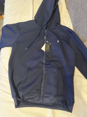 Mörkblå mjukisbyxor från Polo Ralph Lauren - Säljer ett par mörkblå mjukisbyxor från Polo Ralph Lauren med dragsko i midjan och den klassiska broderade loggan på benet. Byxorna är tillverkade i mjuk bomull och har en relaxed passform som är perfekt för chill dagar. Taggen sitter kvar.