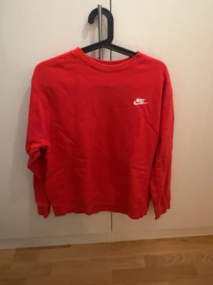Röd sweatshirt från Nike - Säljer en röd sweatshirt från Nike med klassisk logga i vitt på bröstet. Tröjan har rund hals och långa ärmar, perfekt för chill eller träning. Mjuk bomullskvalitet och enkel stil som funkar till jeans eller mjukisbyxor.