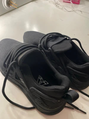 Svarta sneakers, strl 34 - Svarta sneakers från AXE med mesh-ovandel och grovt mönstrad sula. Skorna har snörning och en rund tå, samt detaljer i syntetmaterial. Perfekt för dig som gillar sportig stil och vill ha bekväma skor med cool design. DET ÄR INTE AXEL ARIGATO SKOR!!!