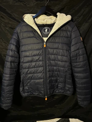 Svart pufferjacka från Save The Duck - Tjena! Säljer nu en riktigt snygg svart pufferjacka med huva från Save The Duck|| fodrad med mjuk teddyfleece i beige|| Jackan är inte fodrad i ärmarna vilket är otroligt skönt för att det inte ska bli för varmt|| Jackan är i storlek M|| inga defekter förutom att teddyfleecen har blivit lite utnött|| hör av dig vid frågor 🙌//StenhamCloset