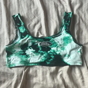 Grön tie-dye topp No Fear x H&M - Säljer en snygg topp från No Fear x H&M med grönt och svart tie-dye mönster. Toppen har breda axelband och en cool No Fear-logga framtill. Perfekt för att ge din outfit en edgy vibe. Väldigt stretchig. Den är mer neon grön i verkligheten  Storlek L Från H&M