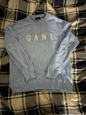 Ljusblå stickad tröja från GANT - Säljer en ljusblå stickad tröja från GANT i storlek S. Tröjan har rund halsringning, ribbade muddar och GANT-bokstäver broderade i vitt framtill. Perfekt för dig som gillar klassisk och clean stil.