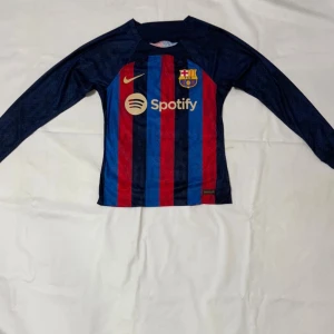 FC Barcelona långärmad matchtröja - Säljer en officiell FC Barcelona långärmad matchtröja från Nike med klassiska blå och röda ränder. Tröjan har klubbmärke på bröstet, guldfärgad Nike-logga och Spotify som sponsor. Materialet är lätt polyester som andas och passar perfekt för fotboll.