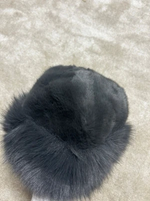 Grå  fluffig pälsväst - Säljer en svart pälsväst med mjuk och fluffig känsla. Västen har en rundad form och är tillverkad i pälsmaterial som ger en lyxig och varm look. Perfekt för dig som vill ha en cool och trendig stil under kyliga dagar.