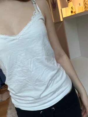 Vit linnetopp med spetskant - Säljer en vit linnetopp med smala justerbara axelband och v-ringad hals. Linnet har en fin spetskant längs halsringningen och är tillverkad i mjuk bomull!