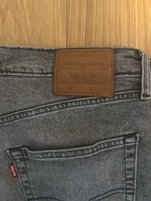 Levi's 502 grå jeans W32 L30 - Säljer ett par grå Levi's 502 jeans med klassisk femficksdesign och rakt snitt. Jeansen har en mörkgrå ton, Levi's patch bak och röd etikett på bakfickan. Materialet är slitstark jeansbomull och passformen är normal med midwaist.