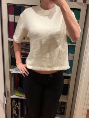 Vit stickad croppad tröja - Säljer en vit stickad tröja med korta ärmar och croppad passform. Tröjan har en rund halsringning och ribbade kanter vid hals och nederkant. Perfekt för dig som gillar en enkel och stilren look med lite edge. Använd 2 gånger! Sitter jätte fint och väldigt varm och skön, passar till allt. 