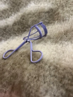 Ljuslila ögonfransböjare från DAAR - Säljer en snygg ögonfransböjare i ljuslila metall från DAAR. Den har mjuka, rundade handtag och en böjd form som gör det enkelt att få till fina fransar. Perfekt för att ge fransarna extra lyft och volym. Färgen är trendig och sticker ut i sminkväskan.