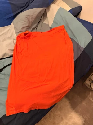 Knallorange långkjol i bomull - Säljer en enkel och snygg långkjol i knallorange färg. Kjolen har rak passform och är gjord i mjukt bomullstyg, perfekt för dig som vill sticka ut med färg. Inga synliga detaljer eller mönster.