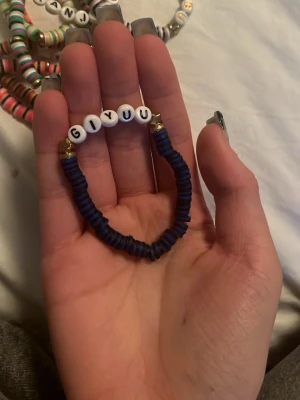 Blått pärlarmband med text Giyuu - Unikt armband med mörkblå platta pärlor och vita bokstavspärlor som stavar 'GIYUU'. Armbandet har även små guldfärgade detaljer vid ändarna. Perfekt för dig som gillar personliga accessoarer och animeinspirerad stil.