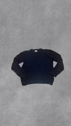 Mörkblå stickad tröja - En enkel och stilren mörkblå stickad tröja med rund hals och långa ärmar. Tröjan har ribbade muddar vid ärmslut och nederkant, vilket ger en klassisk look. Perfekt att matcha med jeans eller kjol för en avslappnad stil.