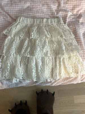 Vit volangkjol i spets från Zara - Supersöt vit kjol från Zara med flera lager volanger och spetsdetaljer. Kjolen har elastisk midja och är perfekt för dig som gillar romantisk och feminin stil. Passar till många olika looks och är lätt att matcha.