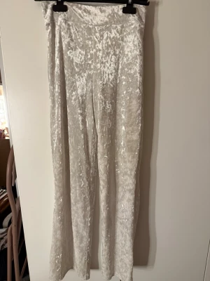 Vita mjukisbyxor i krossad sammet - Säljer ett par vita mjukisbyxor i krossad sammet med rak passform. Byxorna har en mjuk och glansig yta som ger en lyxig känsla. Perfekta för dig som vill ha något bekvämt men ändå stilrent. Passar till chill dagar eller när du vill vara extra cozy.