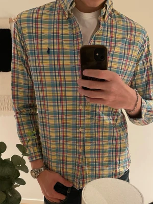 Rutig skjorta från Polo Ralph Lauren - Färgglad rutig skjorta från Polo Ralph Lauren i slim fit-modell. Skjortan har långa ärmar, klassisk krage och knappar framtill. Materialet är mjuk bomull och färgerna går i blått, gult, rött och vitt. Perfekt för dig som gillar en preppy stil.