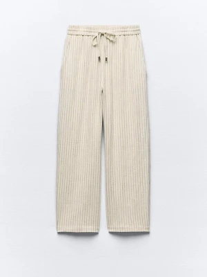 Beige randiga linnebyxor från Zara - Beiga linnebyxor från Zara med tunna svarta ränder och avslappnad passform. Byxorna har resår och snörning i midjan samt raka, vida ben. Perfekta för en chill och stilren look.