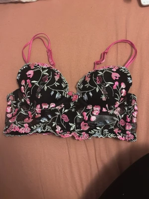 Svart balconette-push up bh med blommig spets - Snygg svart balconette-push up bh med broderade blommor i rosa, grönt och vitt samt spetsdetaljer längs kanterna. 
