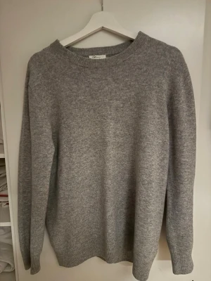 Grå stickad merinoull tröja  - En enkel och stilren grå stickad tröja från Garde Frisch. Tröjan har rund halsringning, långa ärmar och ribbade muddar vid hals, ärmslut och nederkant. Perfekt för lager på lager och passar till det mesta.