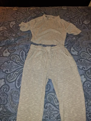 Ribbat loungewear-set - Mysigt loungewear-set i ljusviolett/grått med ribbad struktur. Perfekt för chill dagar hemma. Materialet är mjukt och stretchigt för extra komfort. Tröjan är i storlek M och byxorna i storlek S.