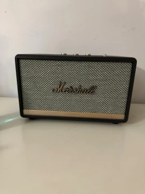 Marshall Acton II trådlös högtalare - Marshall Acton II är en stilren trådlös högtalare i svart med klassisk retrodesign. Fronten har ett metallgaller med Marshall-loggan och ovansidan har guldfärgade reglage för volym, bas och diskant. Högtalaren har robust känsla och ikonisk look. Ny skick.  Finns i Västerås att hämta.  Priset kan diskuteras.