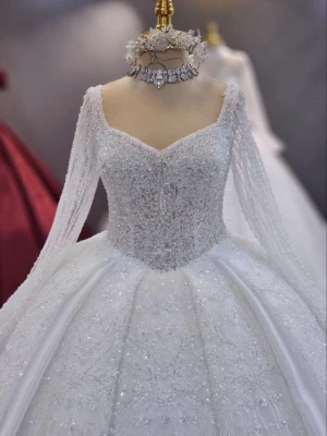 Glittrig vit balklänning med långa ärmar - Magisk vit balklänning med glittrande detaljer, markerad midja och vid kjol. Klänningen har långa, transparenta ärmar och vacker sweetheart-urringning. Toppdelen är täckt av pärlor och paljetter för extra lyxig känsla. Perfekt för dig som vill sticka ut.