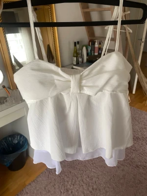Vit linnetopp  - Supersöt vit linnetopp med tunna axelband. Toppen har ett luftigt, dubbellager tyg som ger en flowy känsla. Perfekt för sommarens alla tillfällen och lätt att matcha med både jeans och kjol.