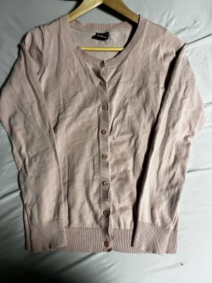 Ljusrosa kofta från Cubus - Söt ljusrosa kofta från Cubus med rund halsringning och knappar framtill. Koftan har långa ärmar och ribbade muddar vid ärmslut och nederkant. Perfekt att slänga över en topp för en chill look.