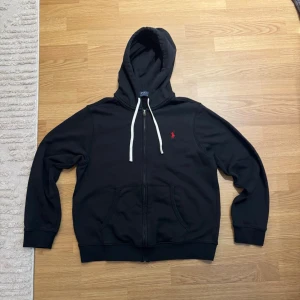 Ralph Lauren Zip-Hoodie - En svart Ralph Lauren zip-hoodie i storlek medium. Endast använd ett fåtal gånger, dvs mycket bra skick.