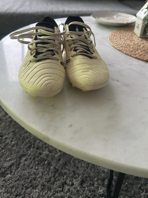 Nike vita fotbollsskor med svart detalj - Säljer ett par vita Nike fotbollsskor med svarta detaljer och snörning. Skorna har en rund tå och är tillverkade i syntetmaterial med klassisk Nike-logga på sidan. Perfekta för dig som vill ha stilrena och funktionella skor på planen.