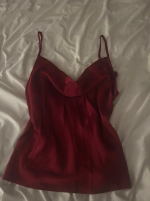 Vinröd satinblus från SHEIN - Snygg vinröd blus i satin från SHEIN med tunna axelband och draperad urringning. Perfekt för att skapa en trendig och elegant look. Materialet är glansigt och mjukt, vilket ger en lyxig känsla.