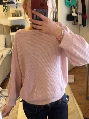 Ljusrosa stickad tröja Vero Moda - Ljusrosa stickad tröja från Vero Moda med avslappnad passform och rund halsringning. Tröjan har långa ärmar och ribbstickade muddar vid ärmslut och nederkant. Perfekt för lager-på-lager och enkel att matcha med jeans eller kjol.