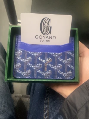 Blå korthållare med mönster - Gjord i läder och väldigt smidig - Säljer en blå korthållare  med ikoniskt grafiskt mönster i vitt och grått. Korthållaren har flera fack och insidan är gul. Tillverkad i skinn och har en riktigt clean och lyxig vibe. Perfekt för dig som vill ha något unikt och stilrent i fickan.